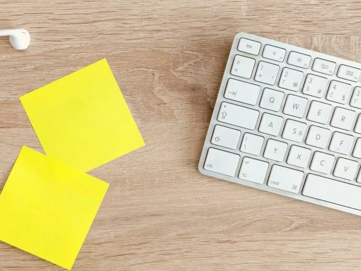 Notas adhesivas amarillas junto a un teclado blanco sobre una mesa de madera